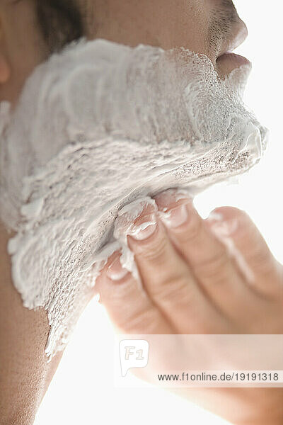 Close up of a young man applying shaving cream on his neck