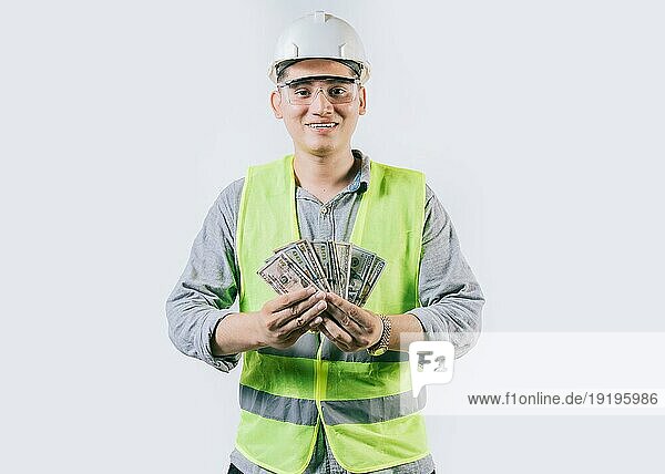 Porträt eines fröhlichen Ingenieurs mit Helm  der Geld hält  isoliert. Fröhlicher männlicher Ingenieur hält Geld auf isoliertem Hintergrund