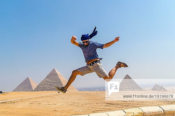 Ein junger Tourist mit blauem Turban und Sonnenbrille hüpft vor Freude bei den Pyramiden von Gizeh  dem ältesten Begräbnisdenkmal der Welt. In der Stadt Kairo  Ägypten  Afrika