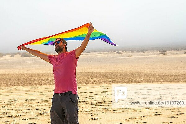 Eine schwule Person mit der LGBT Flagge  die sich mit dem Wind in einer Wüste bewegt  Symbol der Homosexualität  Regenbogenflagge