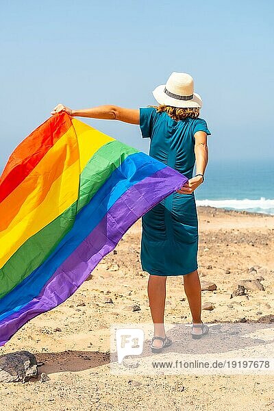 Lgbt Symbol  eine nicht erkennbare lesbische Person mit dem Rücken zugewandt  die in einem grünen Kleid und weißem Hut spazieren geht und die Flagge am Meer schwenkt