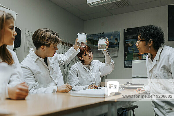 Teacher and students examining chemical in beaker at school laboratory