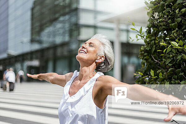 Happy senior woman with outstretched arms in the city