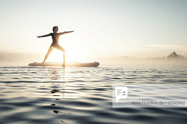 Woman practicing paddle board yoga on lake Kirchsee in the morning  Bad Toelz  Bavaria  Germany