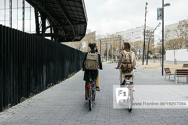 Rear view of couple riding e-bikes in the city talking to each other