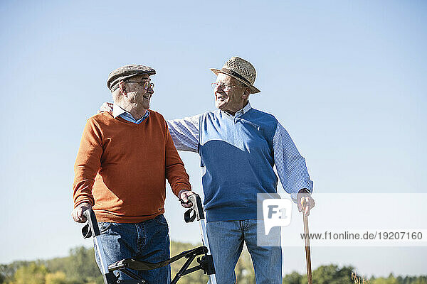 Old friends taking a stroll in the fields with walking stick and wheeled walker  talking about old times