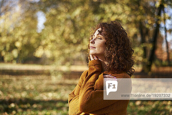 Young redhead woman with eyes closed at autumn park