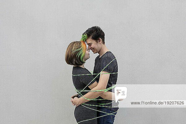 Teenage couple tied up with green rope embracing each other against gray background