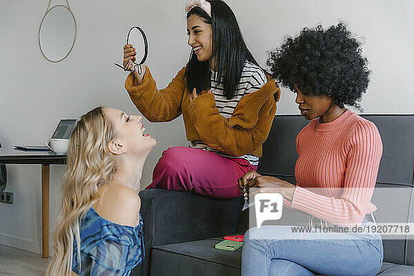 Smiling woman looking at hand mirror next to friends