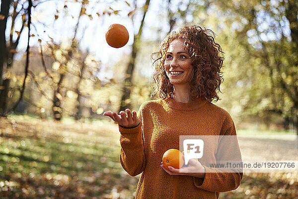 Smiling redhead woman playing with oranges and lemon at autumn park
