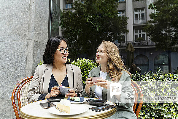 Smiling business partners enjoying coffee sitting at sidewalk cafe