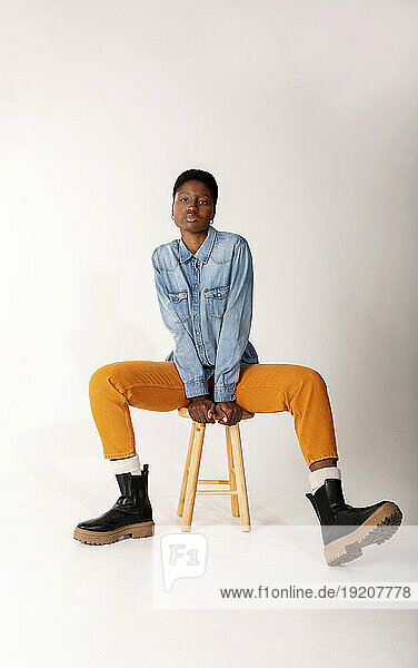 Young woman sitting on stool against white background
