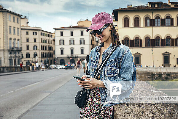 Smiling woman leaning on wall and using smart phone