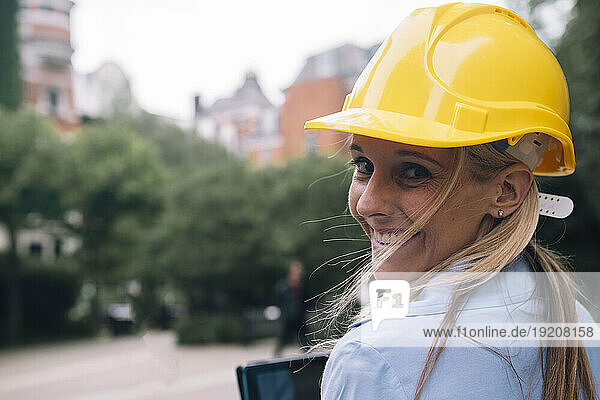 Happy engineer looking over shoulder wearing yellow hardhat