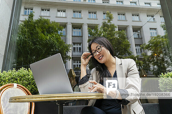 Smiling businesswoman working with laptop at sidewalk cafe