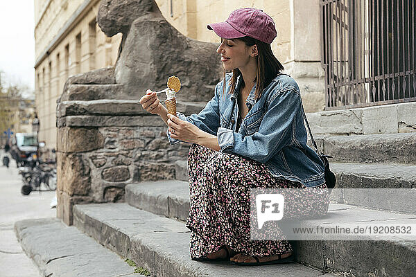 Smiling woman eating ice cream sitting on steps