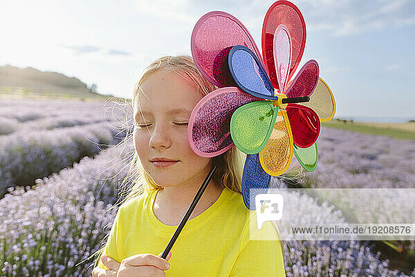 Smiling girl with eyes closed holding pinwheel toy in lavender field