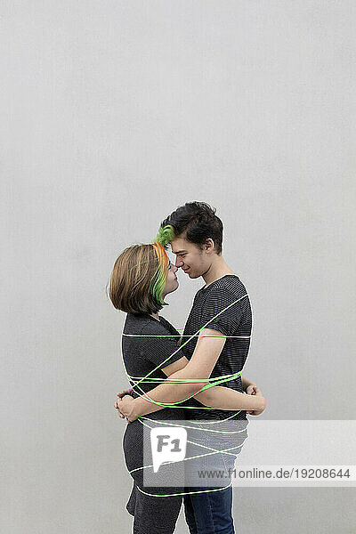 Teenage couple tied up with rope embracing each other against gray background