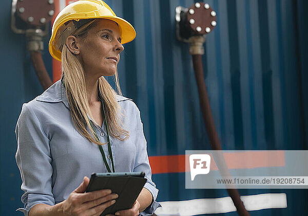 Contemplative engineer wearing hardhat holding tablet PC