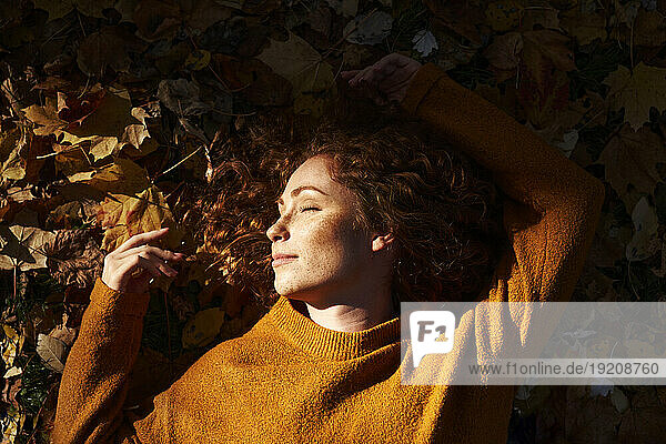 Redhead woman sleeping on autumn leaves at park