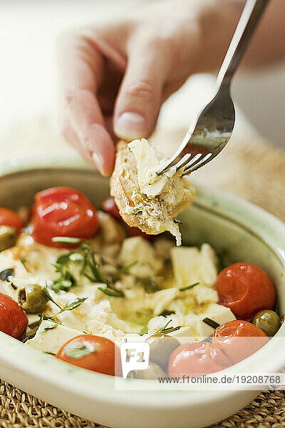 Hand of person eating baked feta cheese with olives  cherry tomatoes and herbs