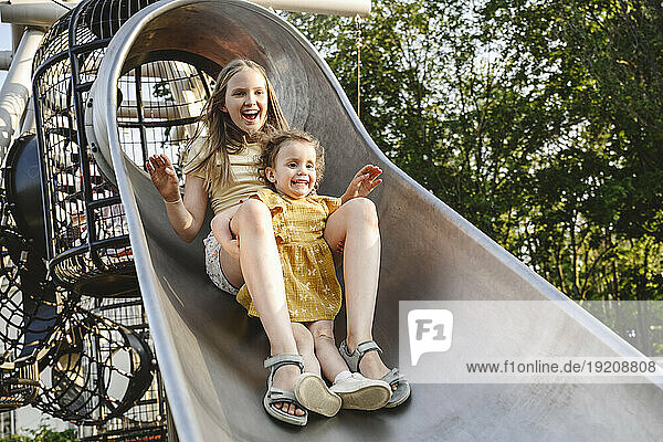 Happy siblings playing on slide at park
