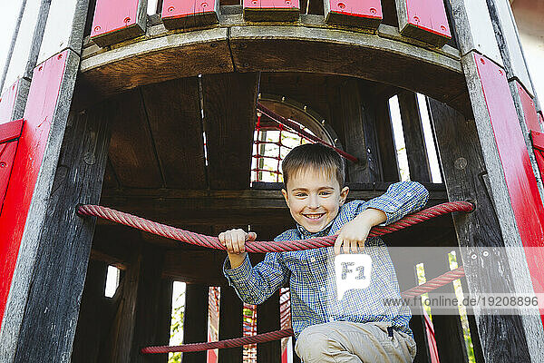 Smiling boy sitting on outdoor play equipment in playground