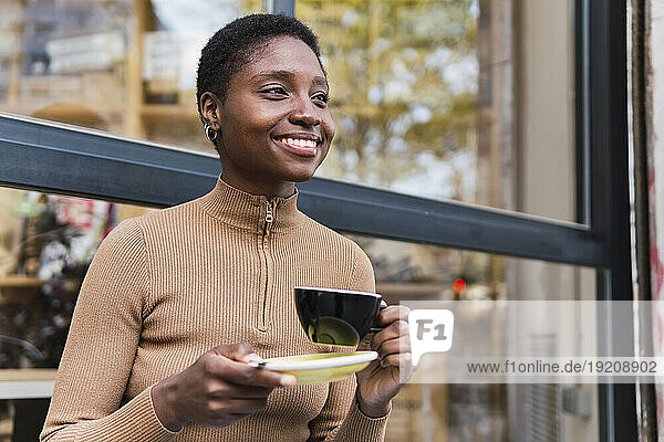 Smiling young woman with coffee cup in front of glass window