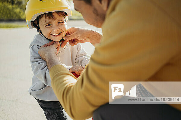Father tying helmet on smiling son