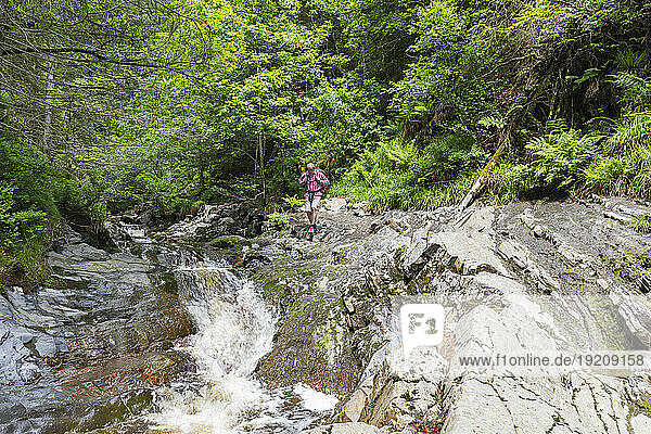 Senior man hiking on rocks near river in forest