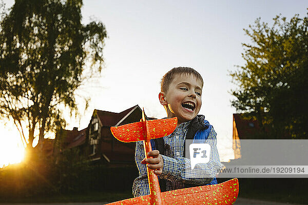 Smiling boy holding toy airplane at sunset