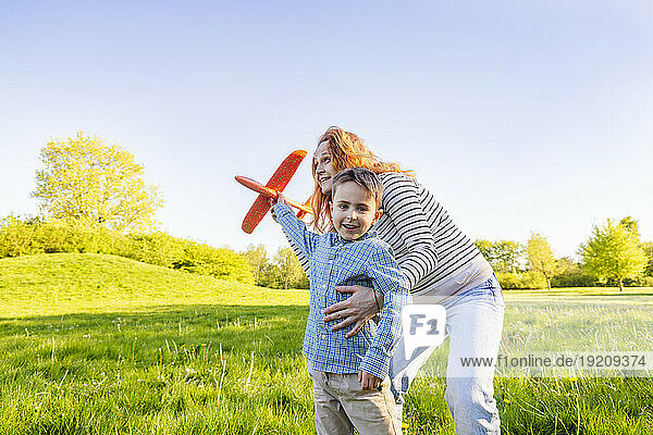 Smiling mother and son playing with toy airplane in garden