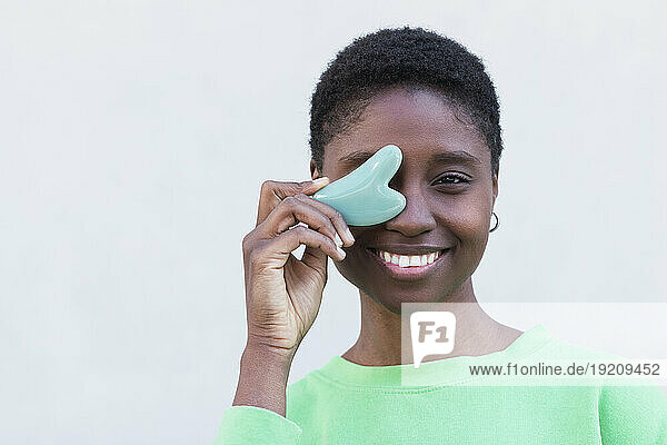 Happy woman with gua sha against white background