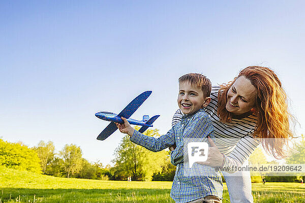 Smiling mother holding son playing with toy airplane