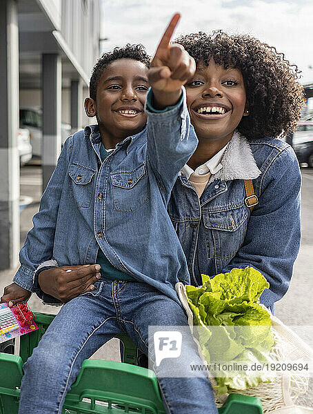Happy woman with boy sitting in shopping cart and gesturing