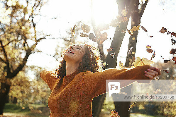 Redhead woman with arms outstretched enjoying autumn leaves falling at park