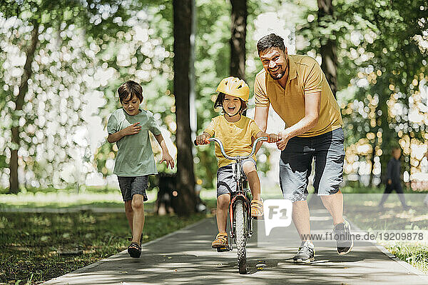 Happy father helping son to ride bicycle in park