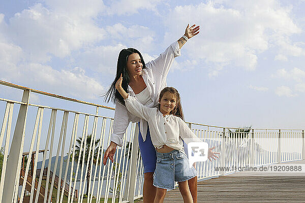 Happy mother and daughter dancing with arms raised on sunny day