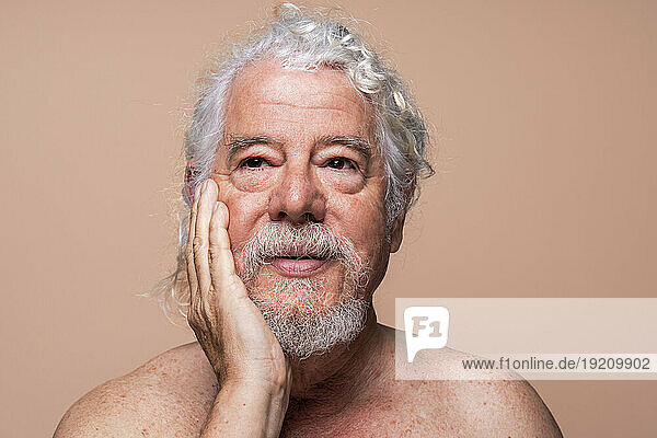 Senior man touching face against beige background