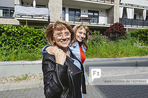 Smiling daughter with arms around mother near residential area