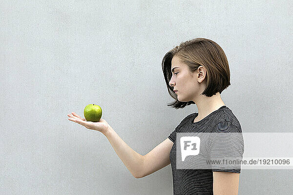 Teenage girl holding green apple against gray background