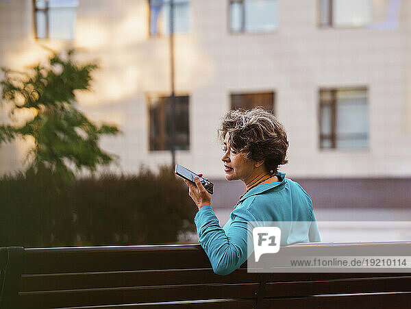 Businesswoman talking through speaker phone sitting on bench