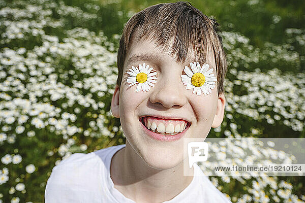 Happy boy with chamomile flowers over eyes