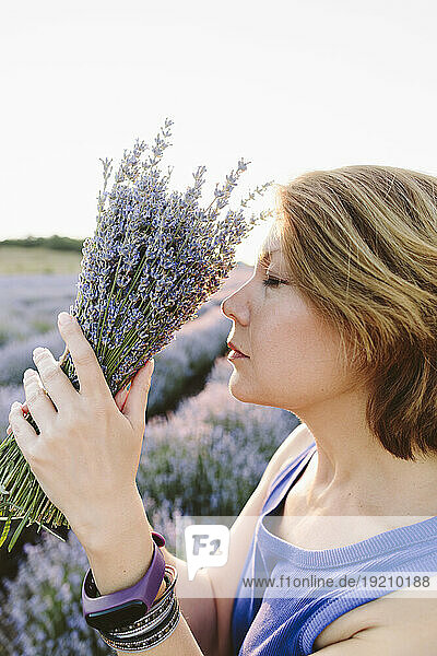 Woman with eyes closed smelling bunch of lavender flowers in field