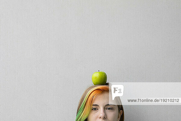 Teenage girl balancing apple on head against gray background
