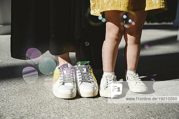 Mother and daughter standing on floor wearing shoes at sunny day