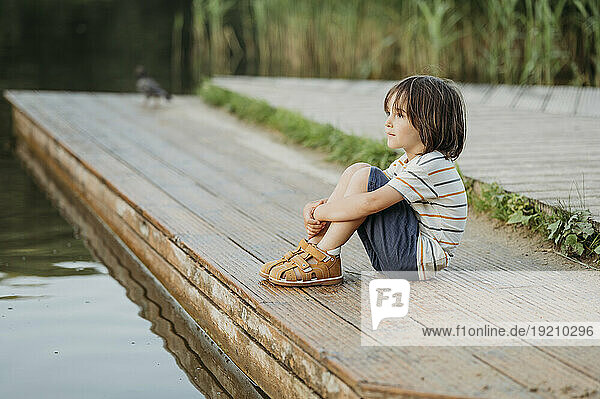 Contemplative boy sitting near lake