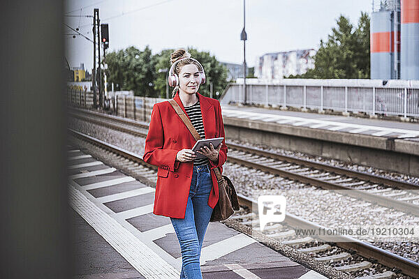 Smiling woman with tablet PC walking on railroad station platform