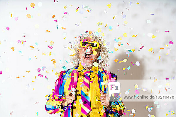 Cheerful senior man with confetti against white background