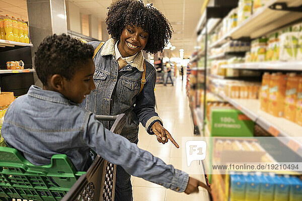 Happy mother and son gesturing towards juice rack in supermarket
